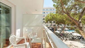 A balcony with white plastic chairs and a table, overlooking a pool area with umbrellas and outdoor seating. - Hotel Best Oasis Park (Salou)