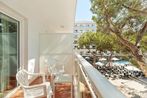 A balcony with white plastic chairs and a table, overlooking a pool area with umbrellas and outdoor seating. - Hotel Best Oasis Park (Salou)