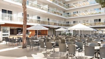 Un espacio de comedor al aire libre con varios niveles, mesas, sillas, una barra y un árbol.