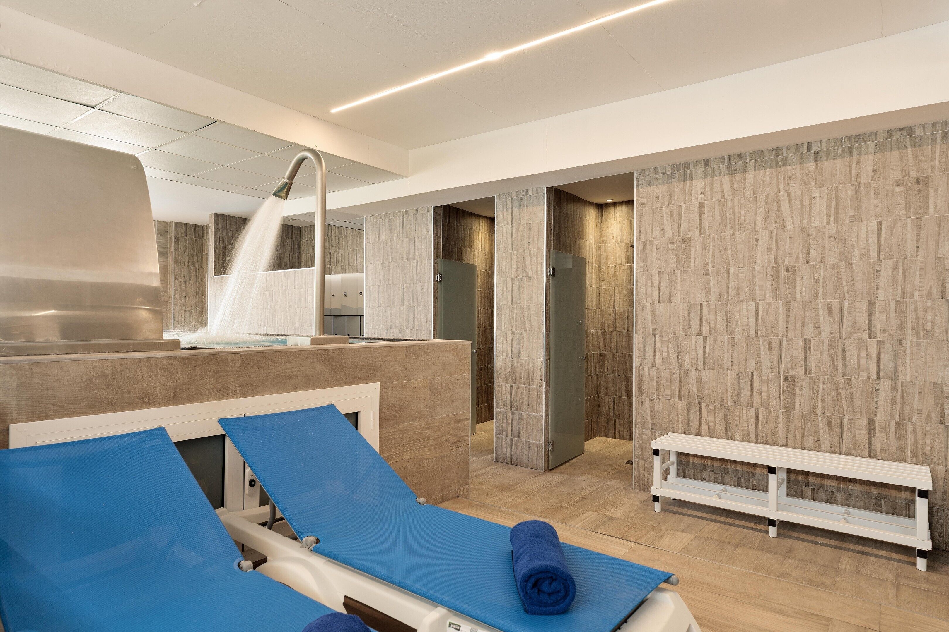 Un spa moderno con un espejo grande, zona de ducha y un banco.