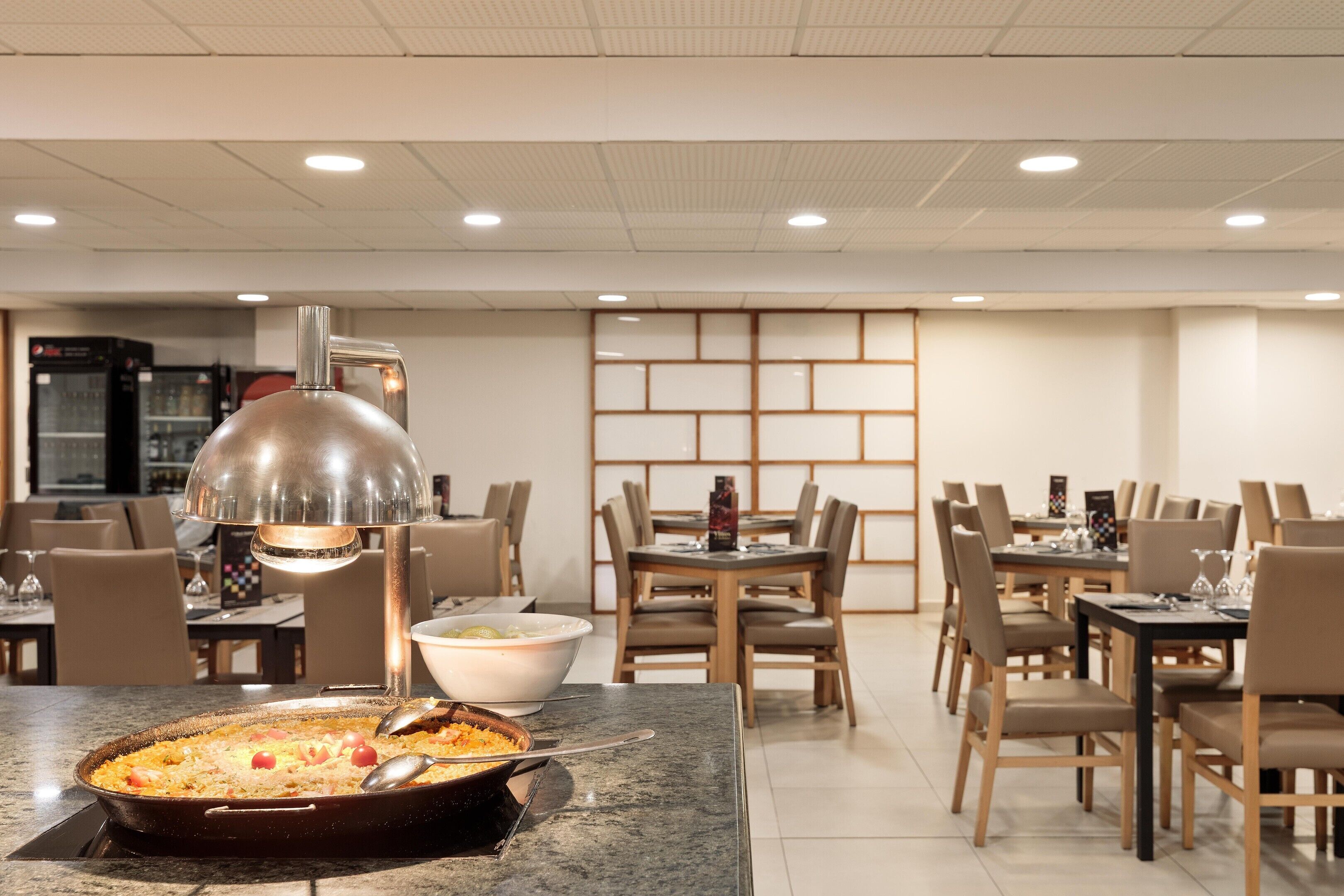 Een eetruimte met tafels, stoelen, een grote pan eten en een moderne hanglamp.