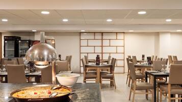 Een eetruimte met tafels, stoelen, een grote pan eten en een moderne hanglamp.