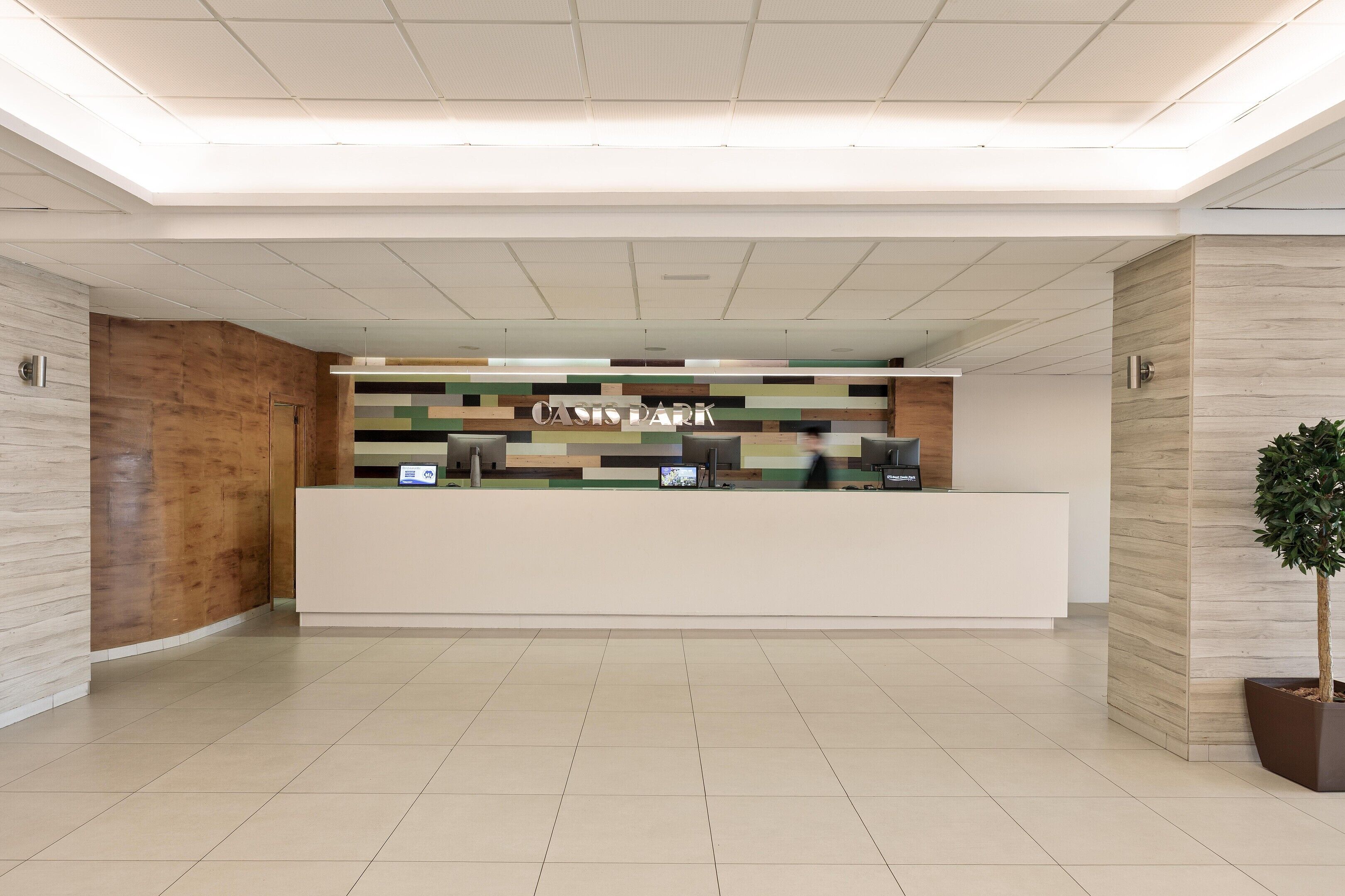 A reception area with a modern design, featuring a reception desk, a digital screen, and a plant.