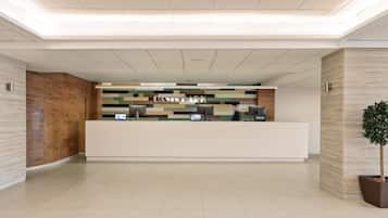 A reception area with a modern design, featuring a reception desk, a digital screen, and a plant.
