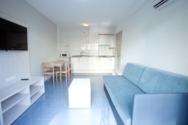 A modern living room with a blue sofa, a white entertainment unit, and a kitchen in the background.