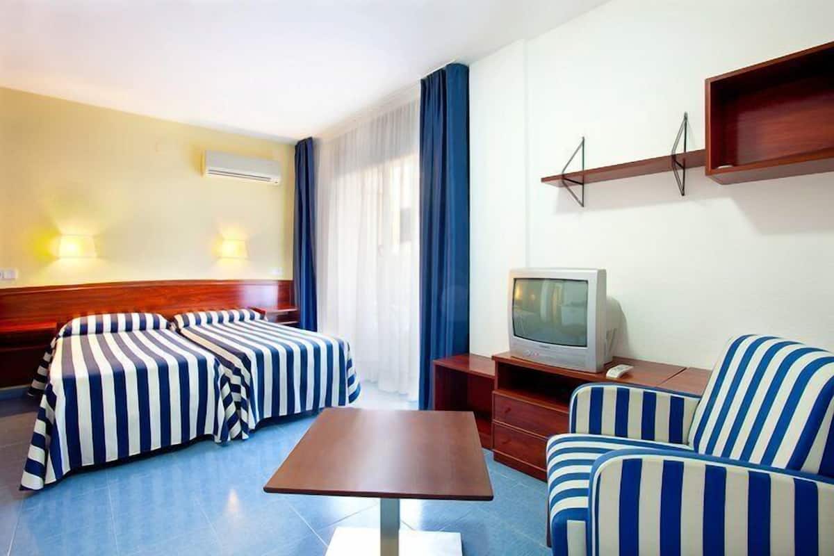 A hotel room with two beds, a TV, a wooden side table, and a small sofa.