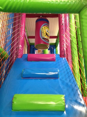Zona de juegos infantiles con tobogán, paredes acolchadas y recinto cubierto de malla.