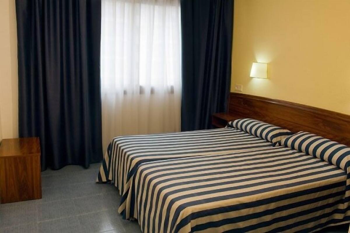 A hotel room with a bed, a nightstand, and a lamp.