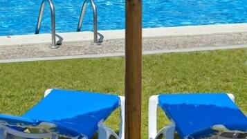 Un área de piscina con dos sillones de playa y una sombrilla de paja.