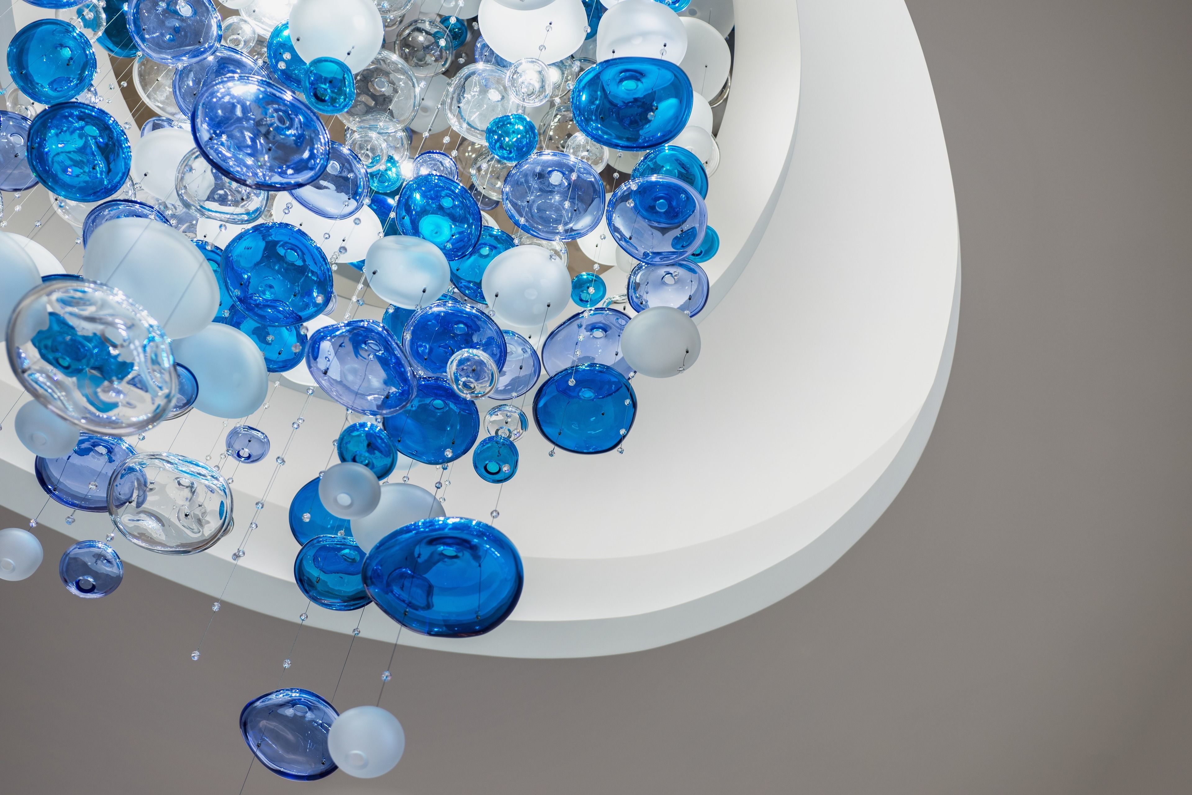 A cluster of transparent glass spheres in various sizes and shades of blue and white, suspended in mid-air.