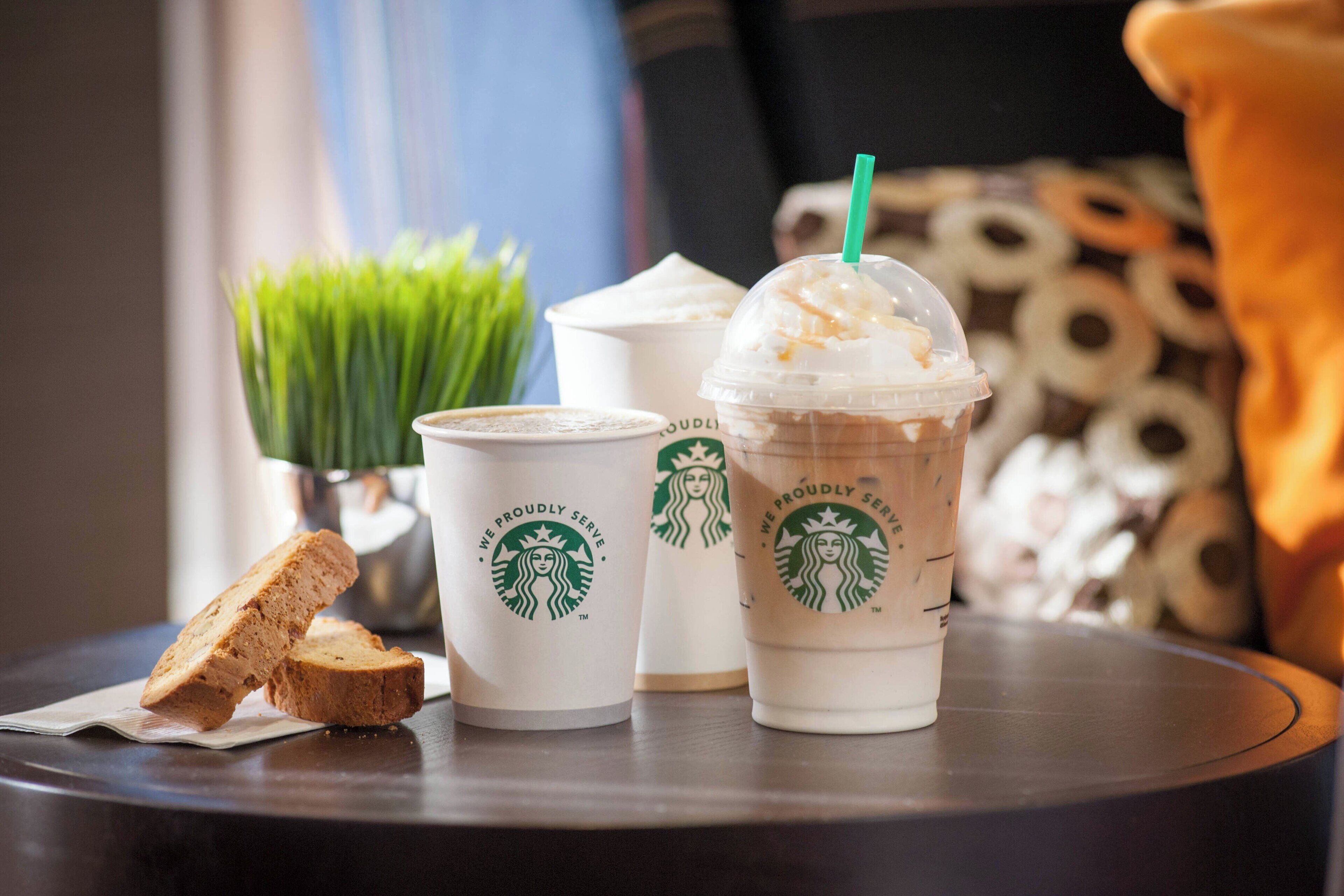 Una mesa con tazas de Starbucks y una rebanada de pan.
