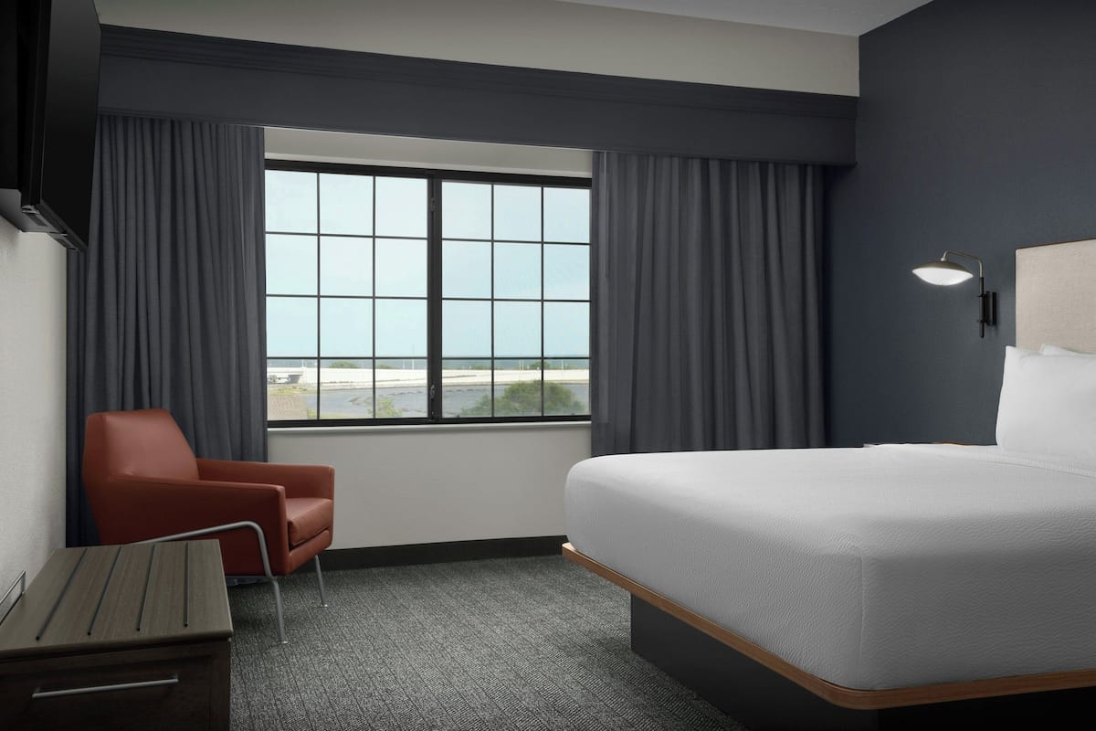 A hotel room with a large bed, a desk, a chair, and a window with a view of the beach.