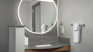 A modern bathroom with a round mirror, a sink, and a towel rack.
