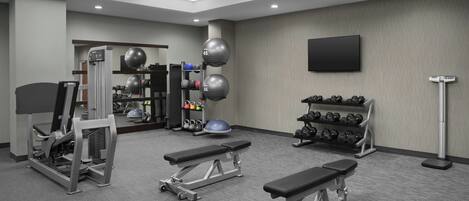 Une salle de sport équipée de machines d’exercice, de bancs, d’un téléviseur fixé au mur et d’un porte-haltères.