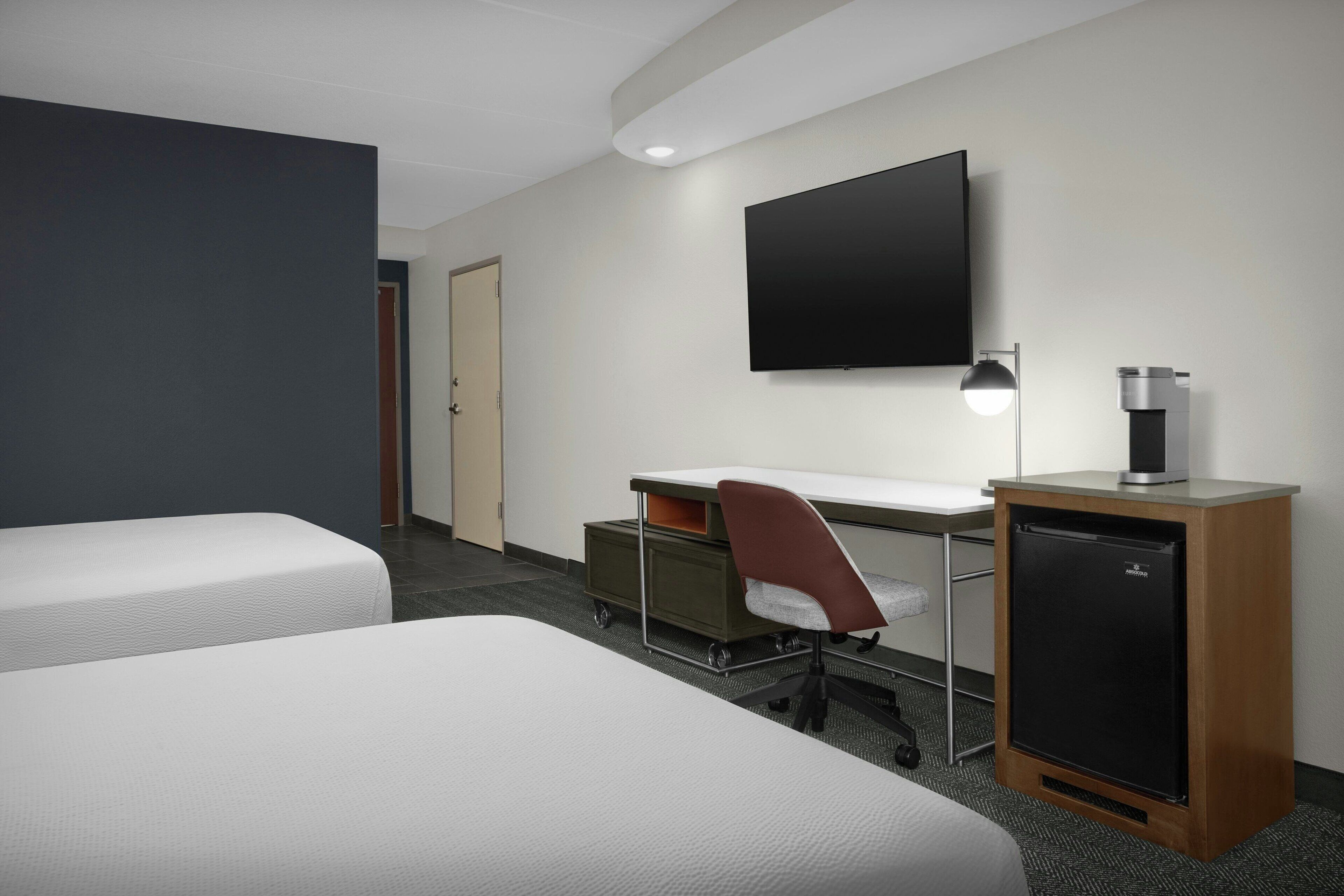 Habitación de hotel con dos camas, un escritorio con silla, televisor, cafetera y mini refrigerador.
