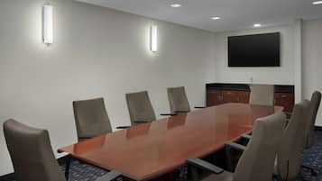 Une salle de conférence avec une longue table en bois, six chaises et un téléviseur à écran plat fixé au mur.
