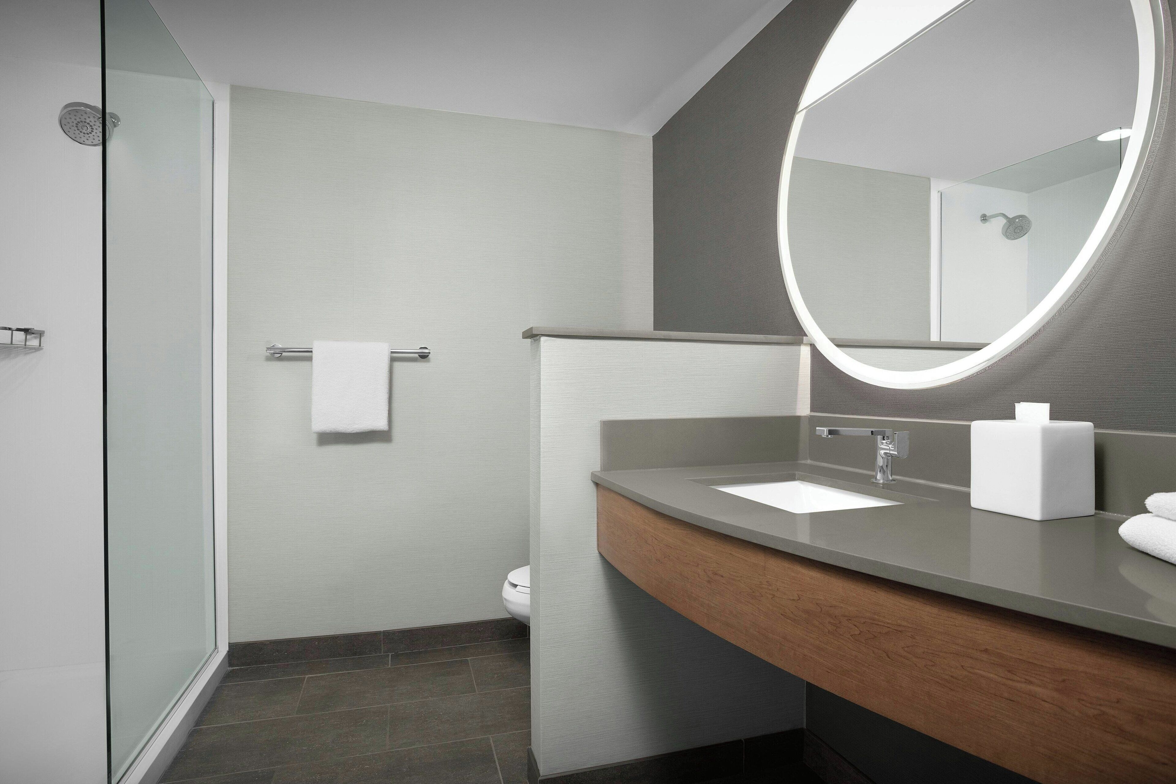 A modern bathroom with a glass shower enclosure, a wooden vanity with a sink, and a large mirror.