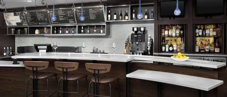 A modern bar area with a long counter, bar stools, and a variety of bottles and glasses.