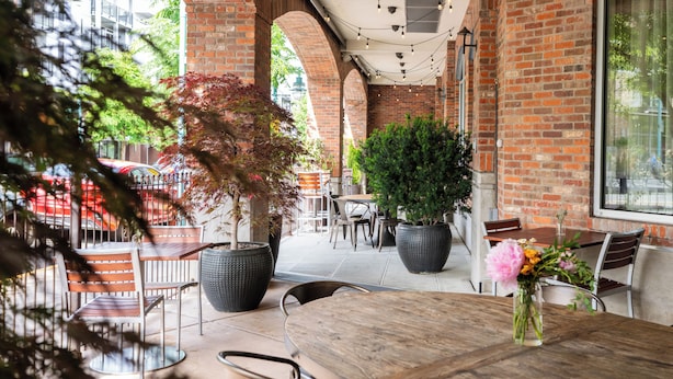 An outdoor patio area with brick walls, wooden tables, and potted plants.