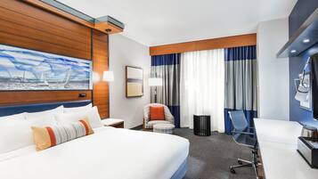 A hotel room with a large bed, a desk, a chair, a small table, and a painting on the wall.