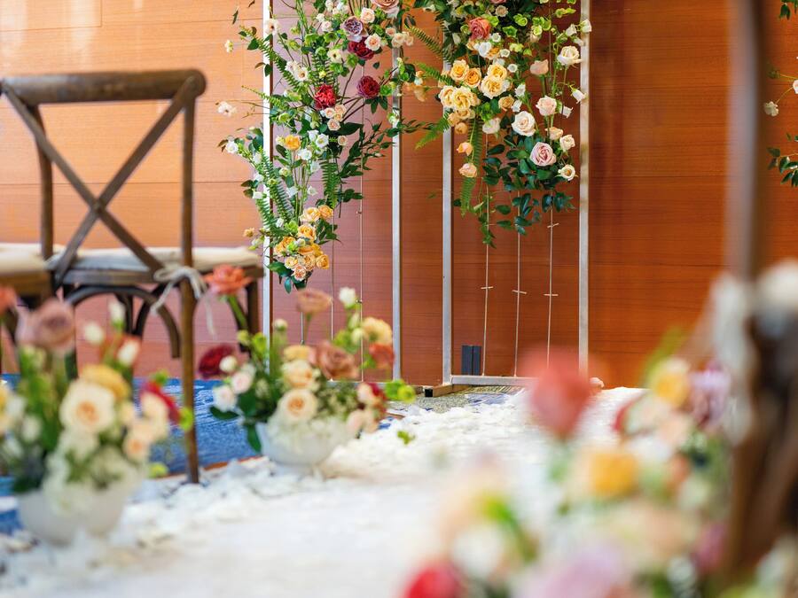 A floral archway with a variety of flowers and greenery, a wooden chair, and a carpeted floor.