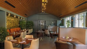 A modern restaurant with wooden ceiling, cushioned seating, and large windows.