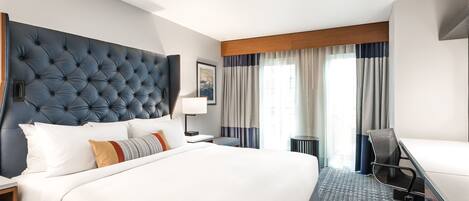 A hotel room with a large bed, a desk, and a view of the outdoors through the window.