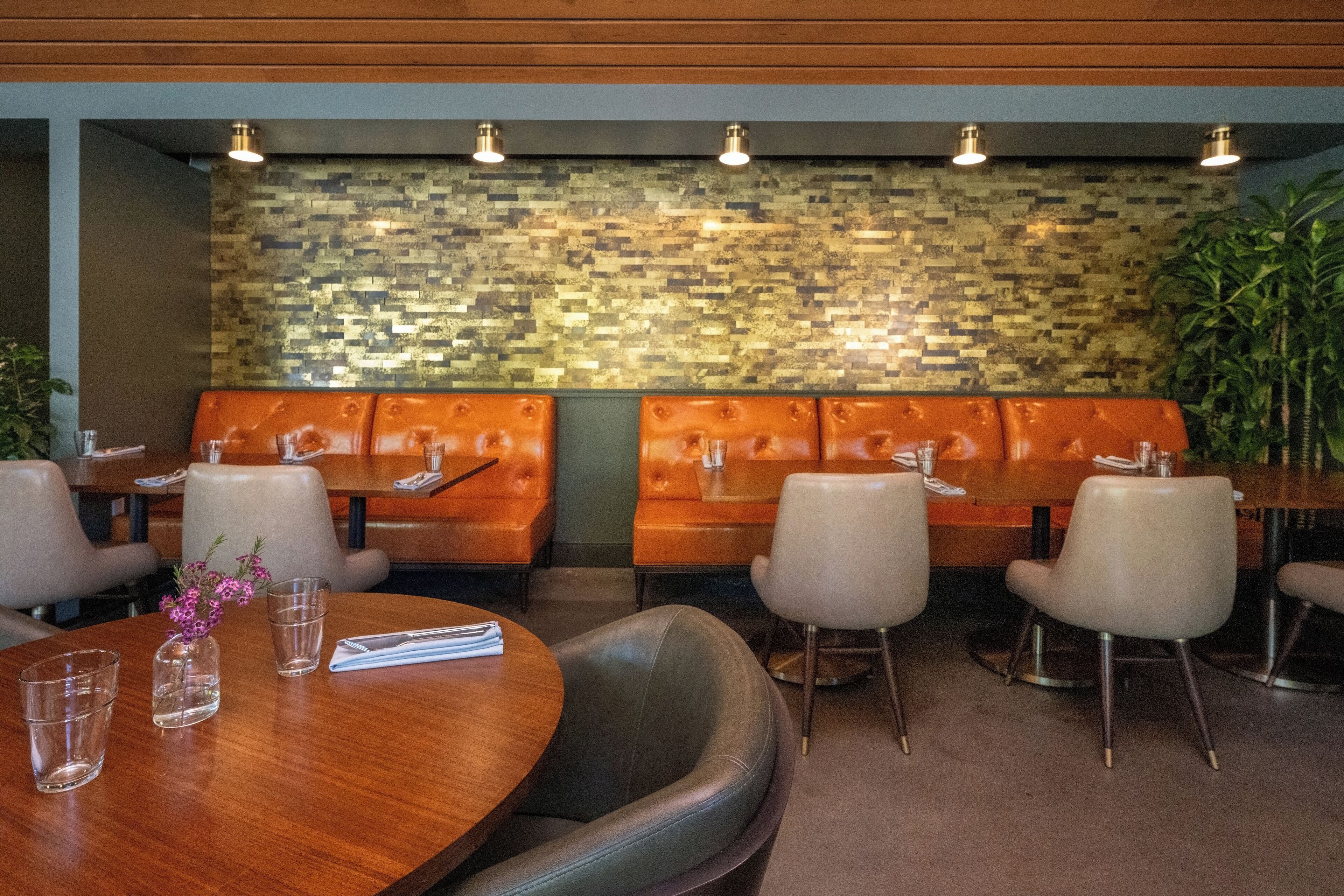A restaurant with booth seating, a mosaic wall, and a wooden table with a vase of flowers.