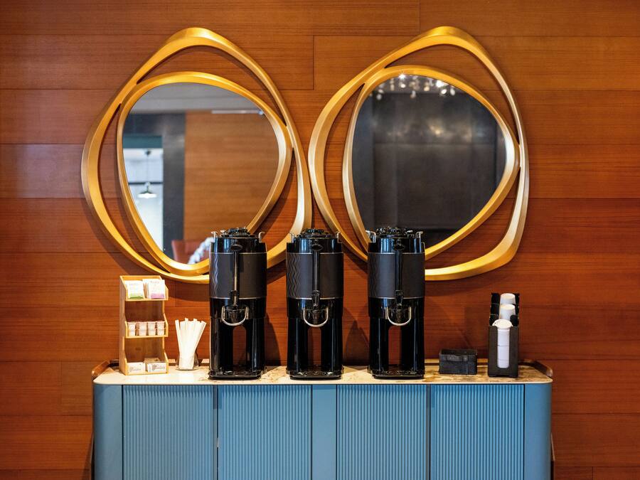 A counter with three coffee makers and a small display of toiletries.