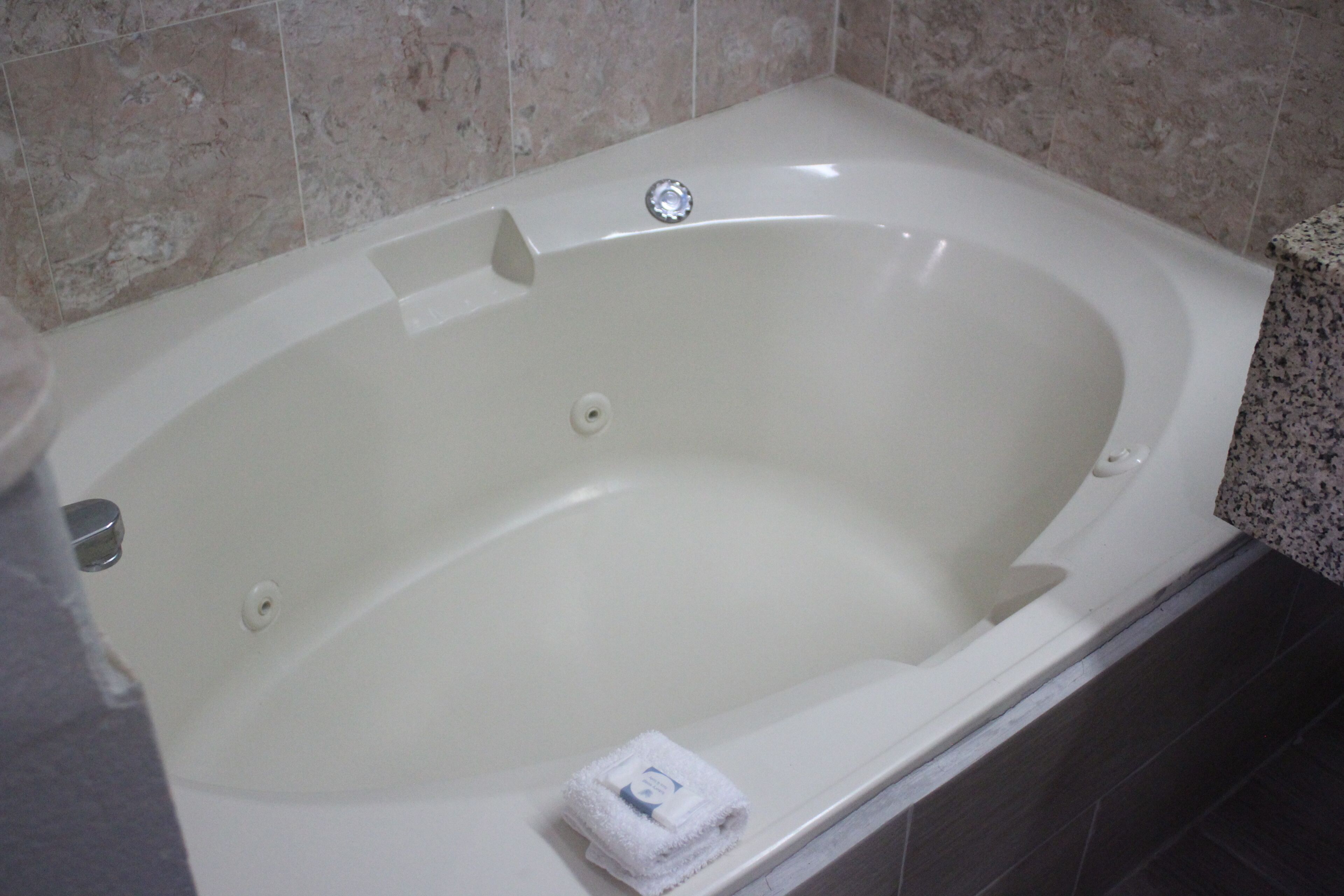 A white bathtub with a single faucet and a drain, set against a tiled wall.