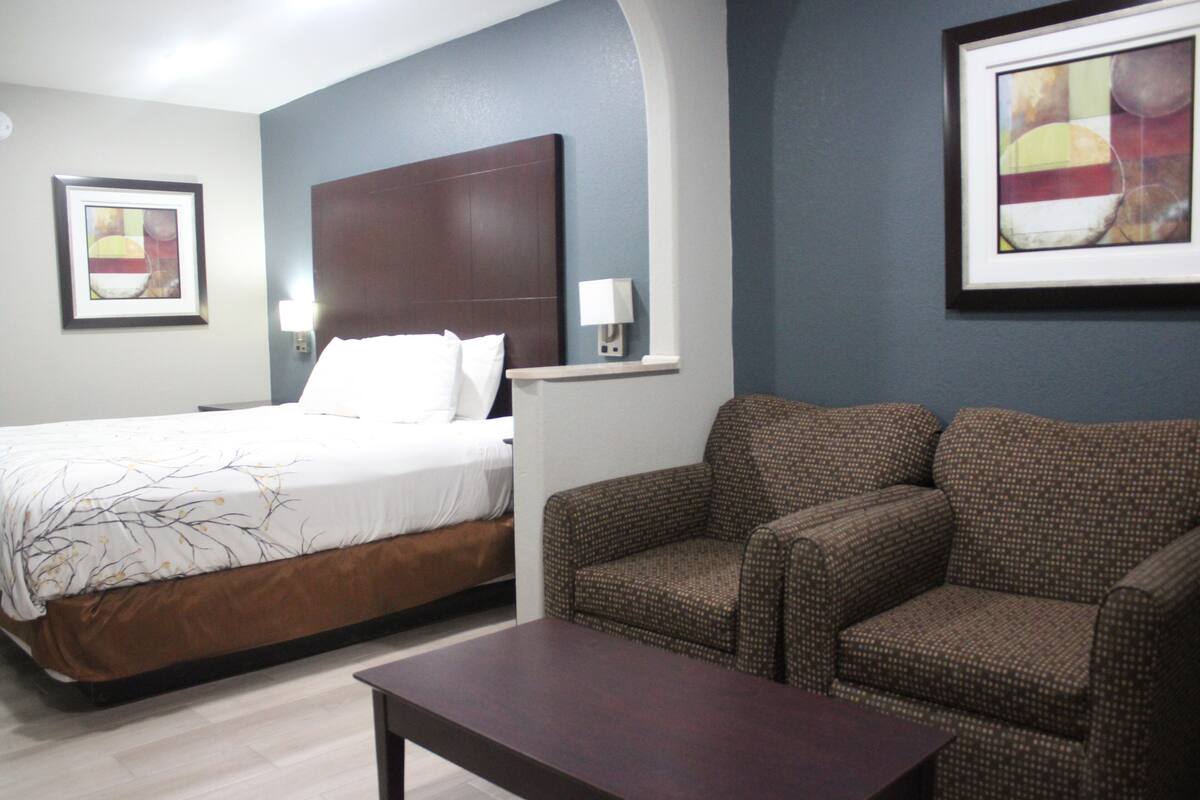 A hotel room with a bed, two armchairs, a small table, and artwork on the walls.