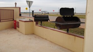 Une terrasse extérieure avec un barbecue et une poubelle.