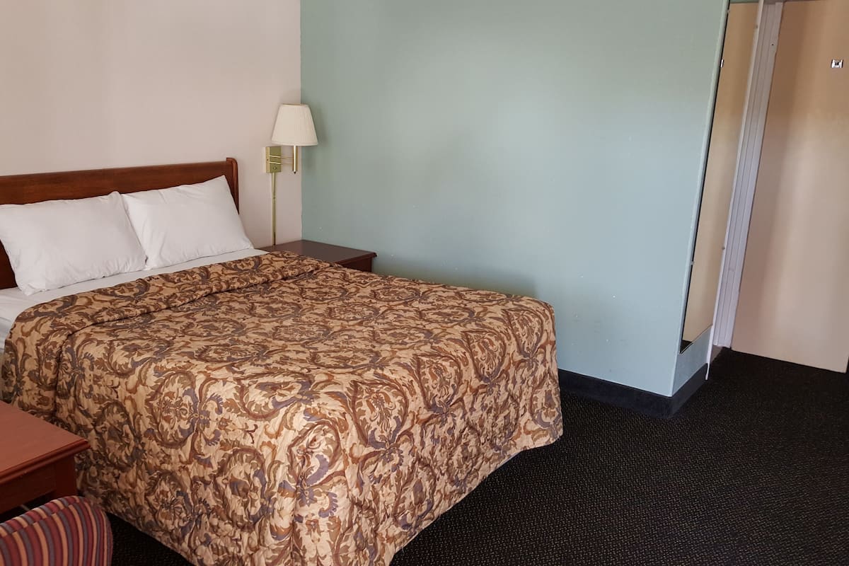 A hotel room with a bed, two bedside tables, a nightstand, a lamp, and a door.