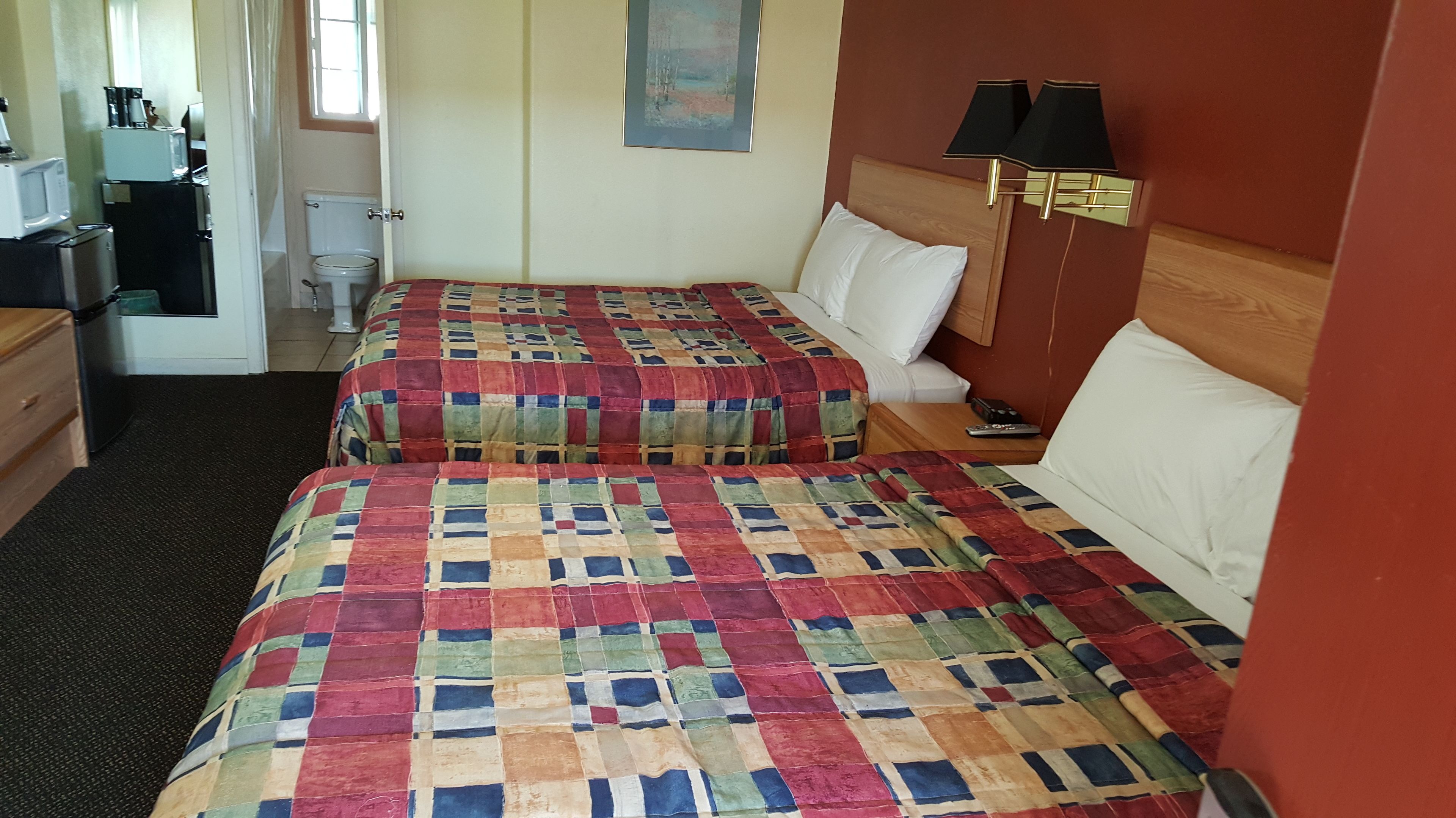 Ett hotellrum med två sängar, ett litet skrivbord med en stol, en toalett och ett fönster.