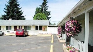 A motel with a parking lot, a red car parked in front, and a flower bed with pink and white flowers on the right side. - Valley Inn (Lebanon)
