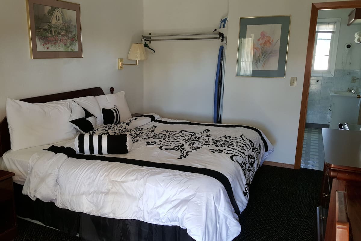 A neatly made bed with a black and white patterned bedspread, a wooden headboard, and a nightstand with a lamp.