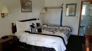 A neatly made bed with a black and white patterned bedspread, a wooden headboard, and a nightstand with a lamp. - Valley Inn (Lebanon)