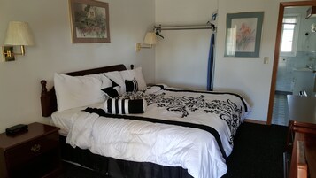 Cama bem arrumada com colcha preta e branca estampada, cabeceira de madeira e mesa de cabeceira com abajur.