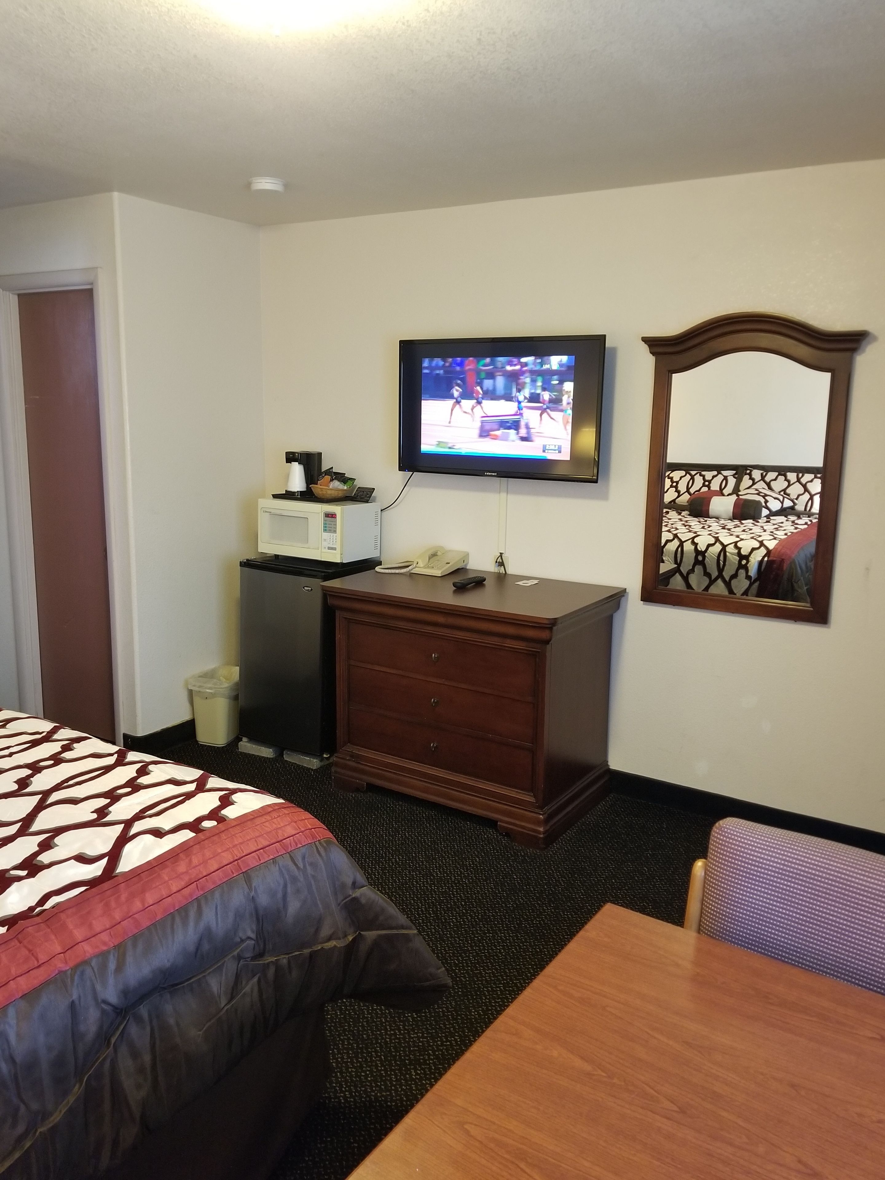 Habitación de hotel con cama, escritorio, televisor, espejo y microondas.
