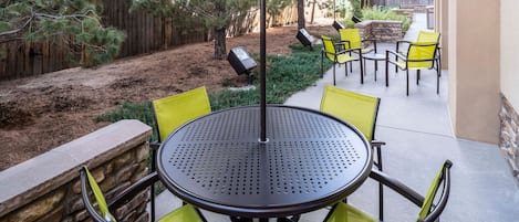 An outdoor patio with a round table and yellow chairs, surrounded by a stone wall and a wooden fence.