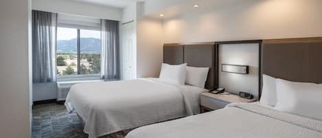 A hotel room with two beds, a large window with curtains, a nightstand with a phone, and a view of the outdoors.