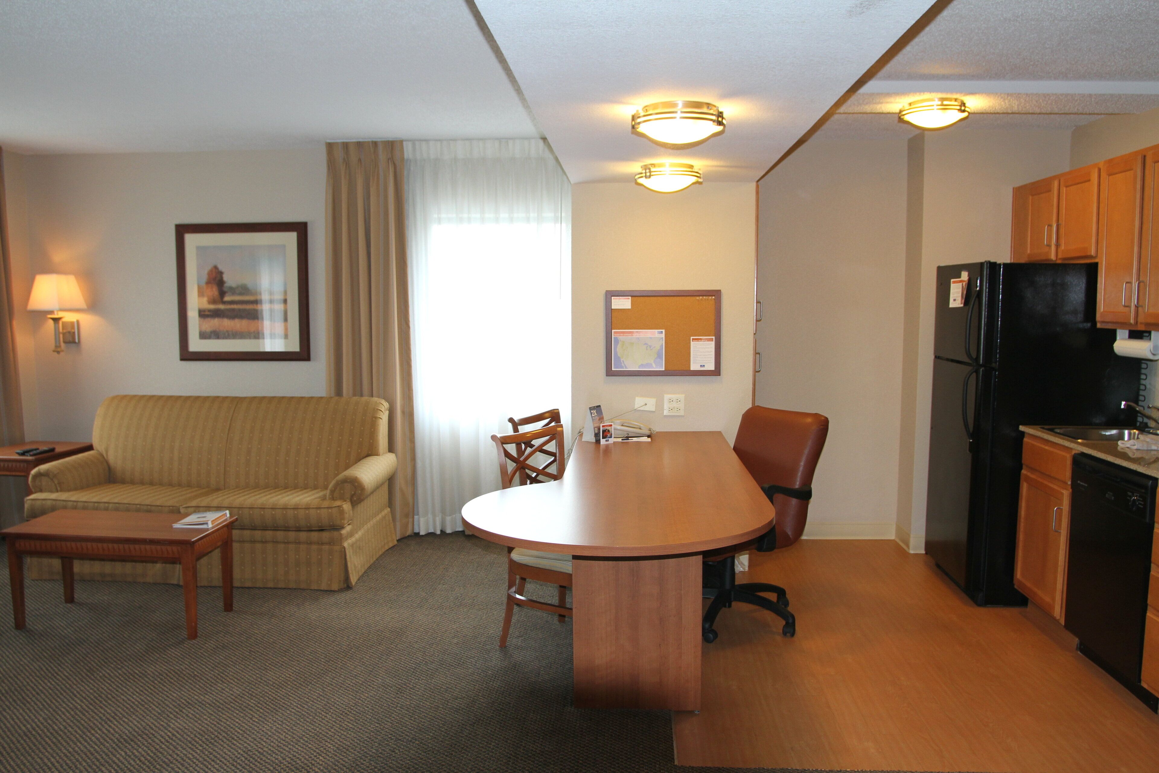 A compact hotel room with a sofa, a dining table, a kitchen area, and a single chair.