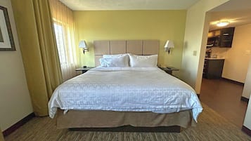 Habitación de hotel con una cama grande, dos lámparas de noche, una mesita de noche, una pequeña mesa y vistas a la cocina.