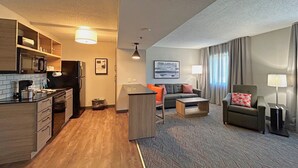 Una habitación de hotel compacta con kitchenette, un sofá, una mesita y una silla.