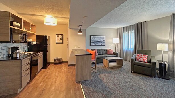 A compact hotel room with a kitchenette, a sofa, a small table, and a chair. - Candlewood Suites Indianapolis Downtown Medical District by IHG (Indianapolis)
