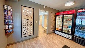Un pasillo con un panel decorativo en la pared, un refrigerador de bebidas y estantes con productos envasados.