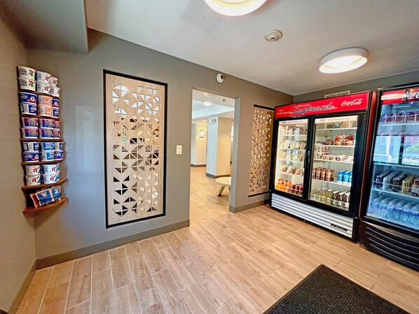 Un pasillo con un panel decorativo en la pared, un refrigerador de bebidas y estantes con productos envasados.