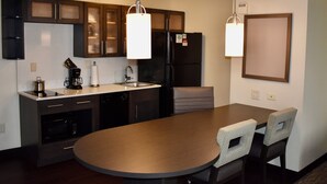 A modern kitchen with dark cabinetry, a central island, and pendant lighting. - Candlewood Suites Indianapolis Downtown Medical District by IHG (Indianapolis)