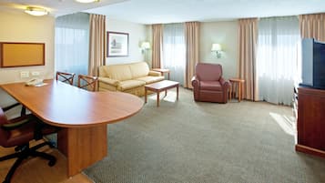 Habitación de hotel con un escritorio de madera, dos sillones, un sofá, un televisor y un cuadro en la pared.
