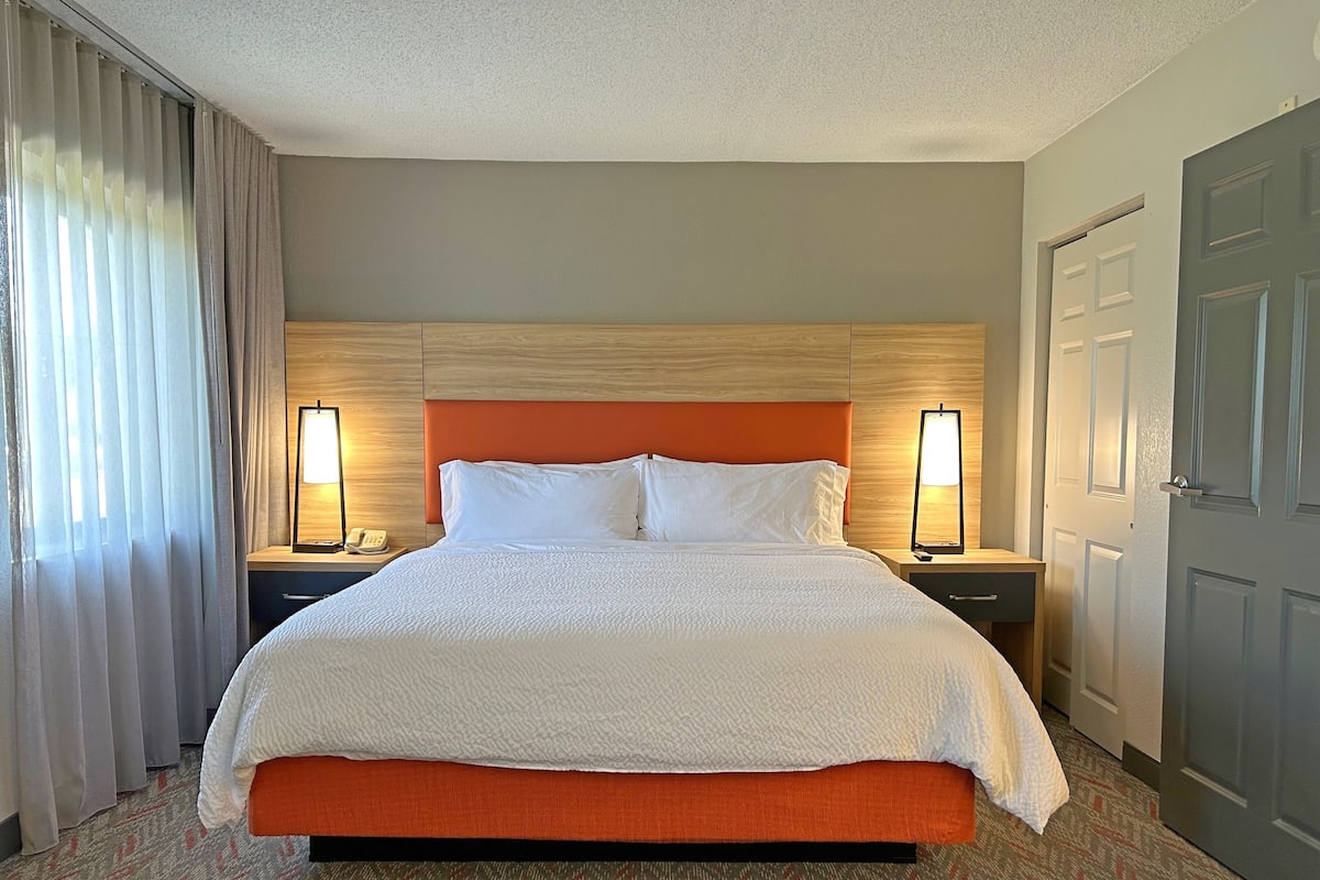 Una habitación de hotel con una cama grande, dos mesitas de noche con lámparas, un teléfono y una puerta.